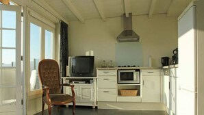 Een kleine keuken met een televisie, magnetron en oven. Er staat een houten stoel bij het raam.