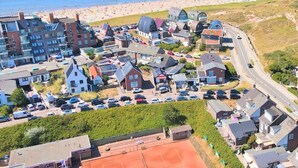 Een woongebied aan de kust met een mix van moderne en traditionele huizen, een strand op de achtergrond en een weg die door de buurt loopt.