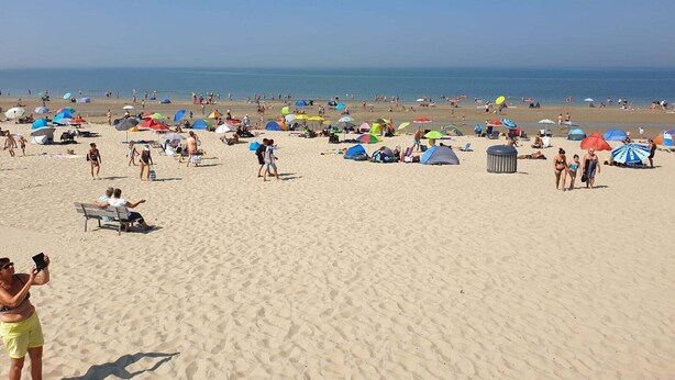 Uma praia arenosa com pessoas, guarda-sóis e tendas.
