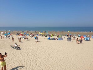 A sandy beach with people, umbrellas, and tents.