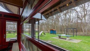 Quarto com uma grande janela com vista para um parque que inclui um parquinho, um banco e uma mesa de piquenique.
