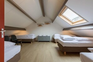 A small, well-lit attic bedroom with two beds, a desk, and a skylight.