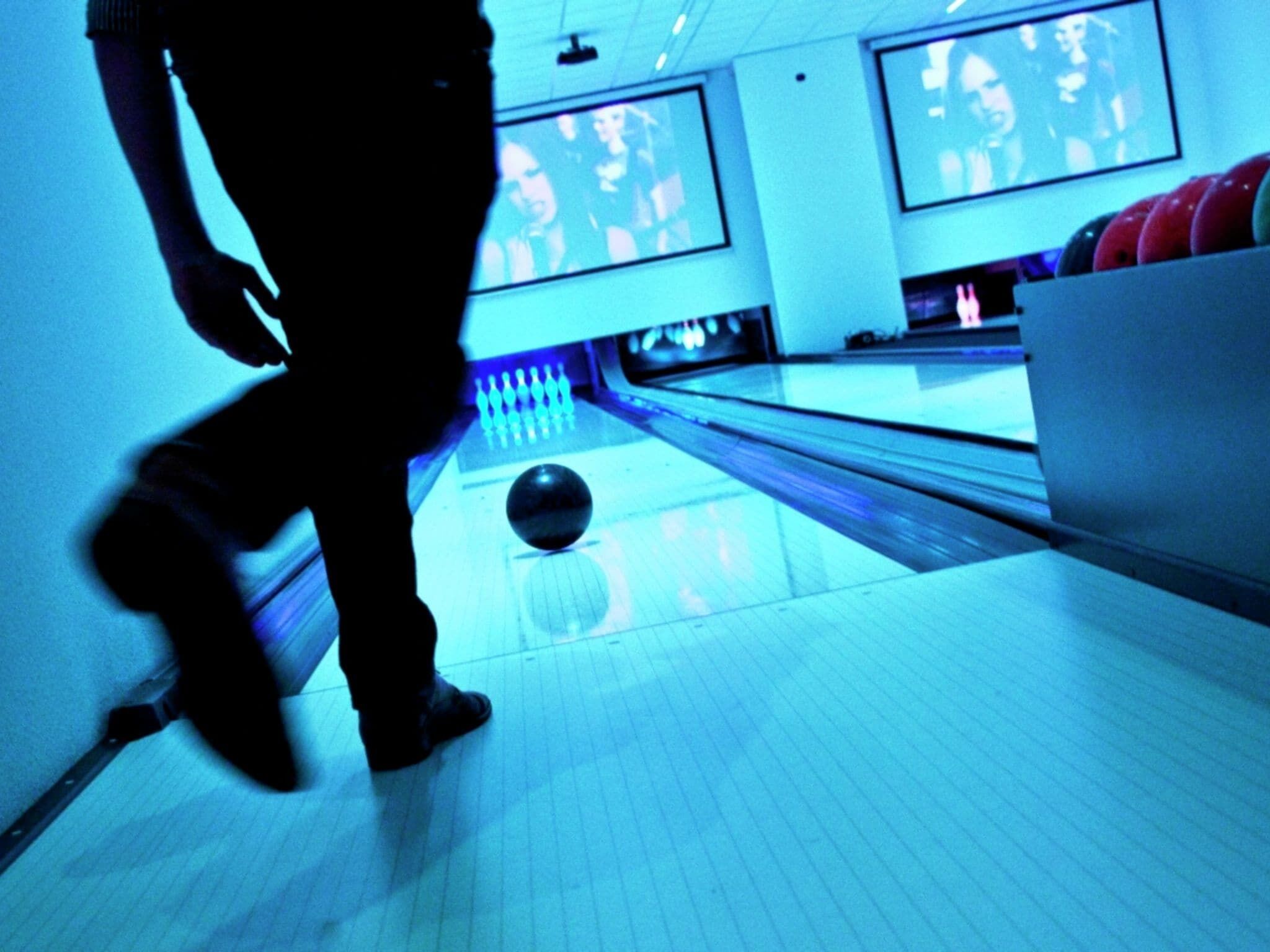 A bowling alley with lanes, pins, and a bowling ball in motion.