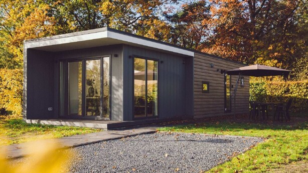 Une maison moderne de plain-pied, dotée de grandes fenêtres en verre, d’un toit plat et d’une allée gravillonnée.