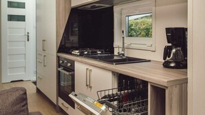 Une cuisine compacte équipée d’un lave-vaisselle, d’une machine à café et d’une fenêtre donnant sur un espace verdoyant.