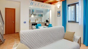 A cozy living room with a sofa, a kitchen area, and a staircase. - Belvilla by OYO Casa Bella (SIRACUSA)