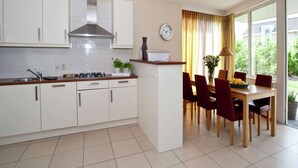 A modern kitchen with white cabinets, a stainless steel range hood, and a dining area with a wooden table and red chairs.