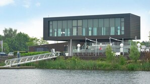 A modern building with large windows, a bridge, and a water body in the foreground.