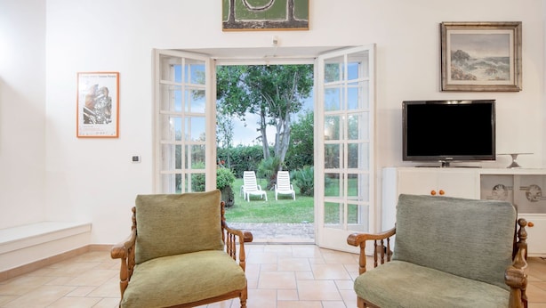 A room with two wooden chairs, a television, and a door leading to a garden. - Beautiful holiday home in Ardea with garden (Ardea (RM))