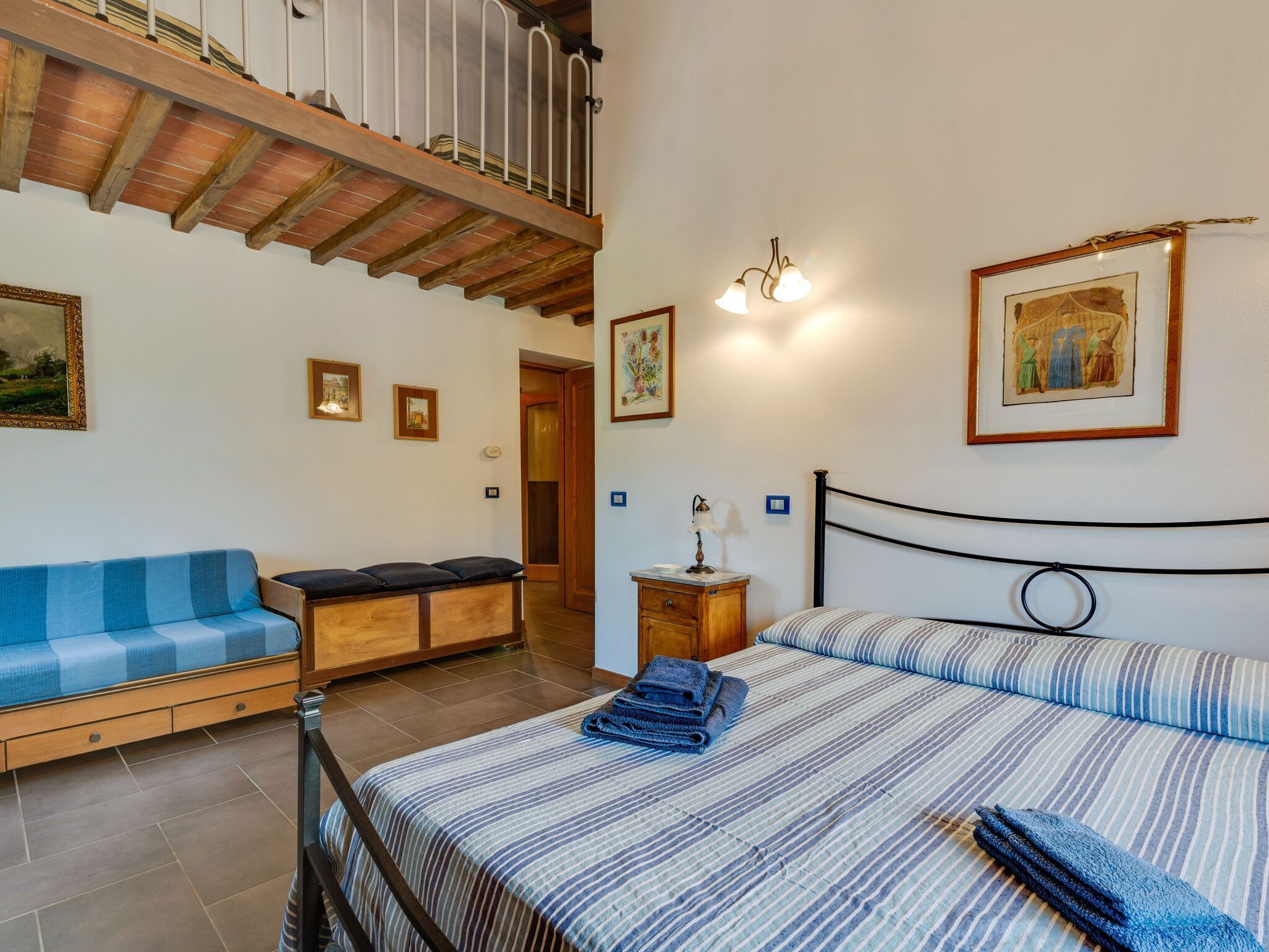 A bedroom with a bed, a blue sofa, a wooden bench, and a staircase.