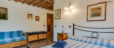 A bedroom with a bed, a blue sofa, a wooden bench, and a staircase.