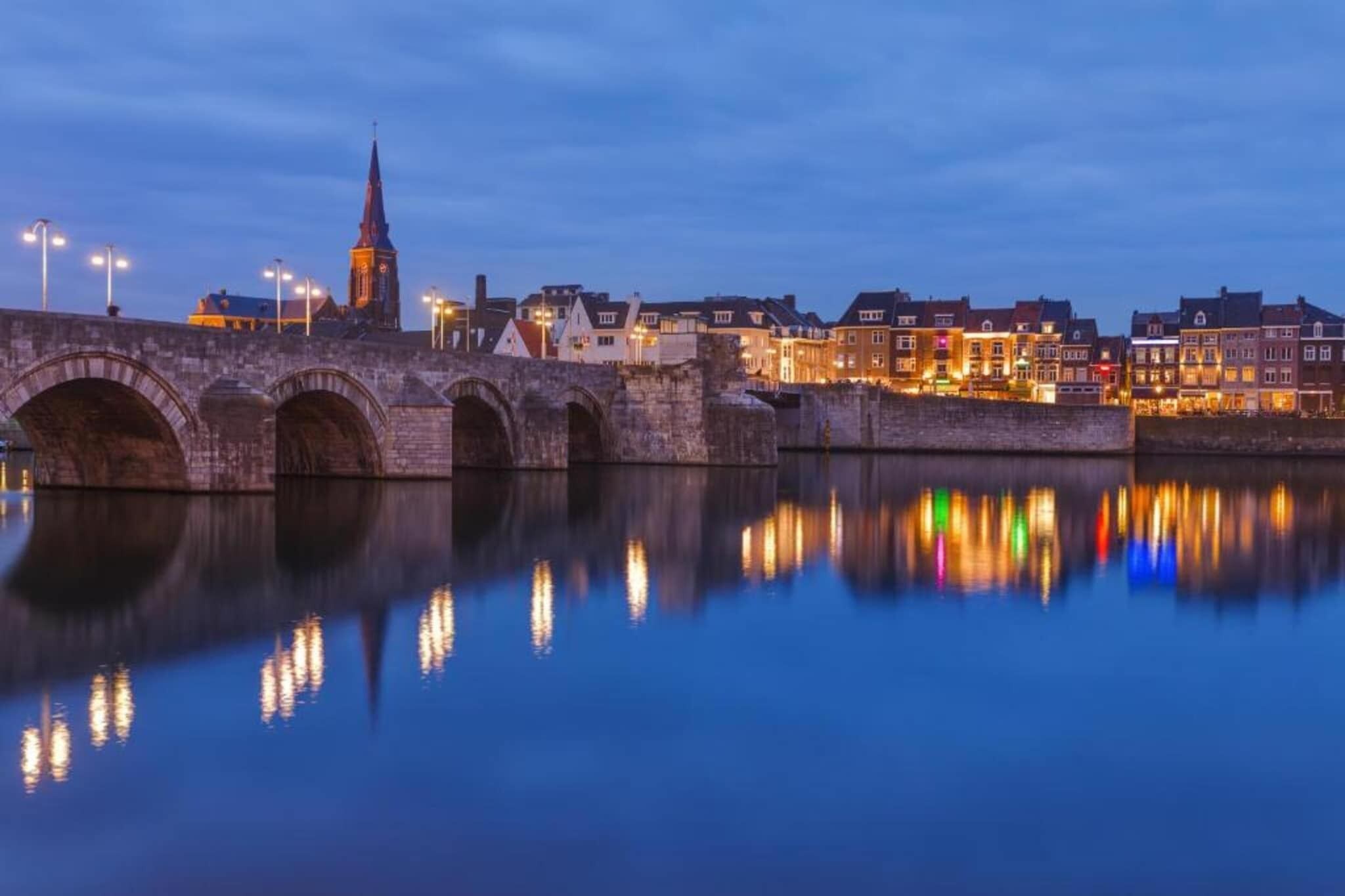 Un puente de piedra con múltiples arcos sobre una superficie acuática tranquila que refleja luces.