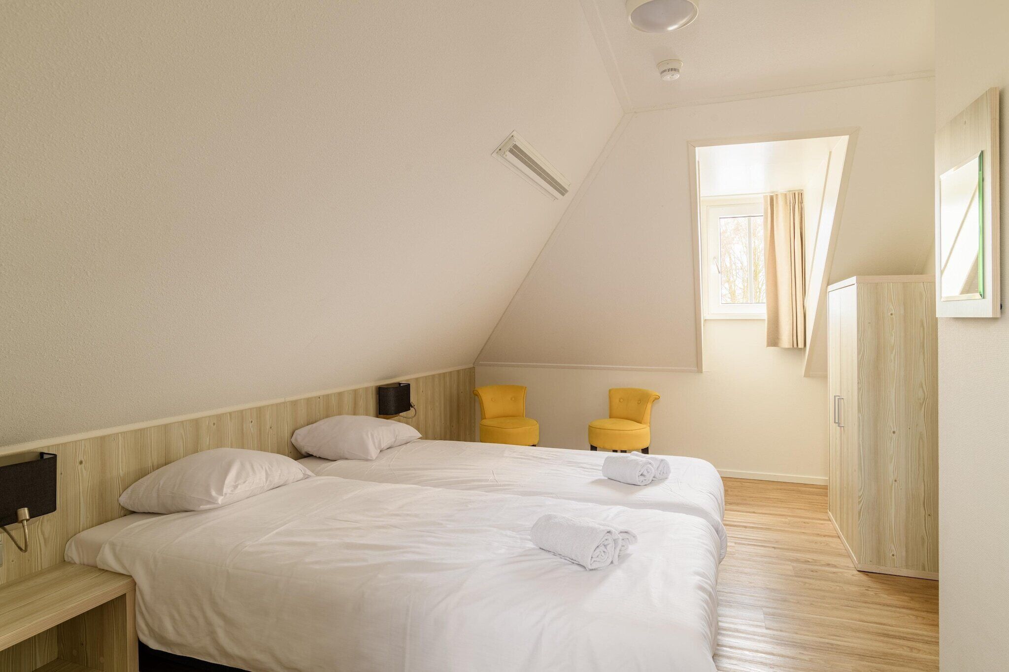 Une chambre avec deux lits, une armoire en bois et une fenêtre avec des rideaux.