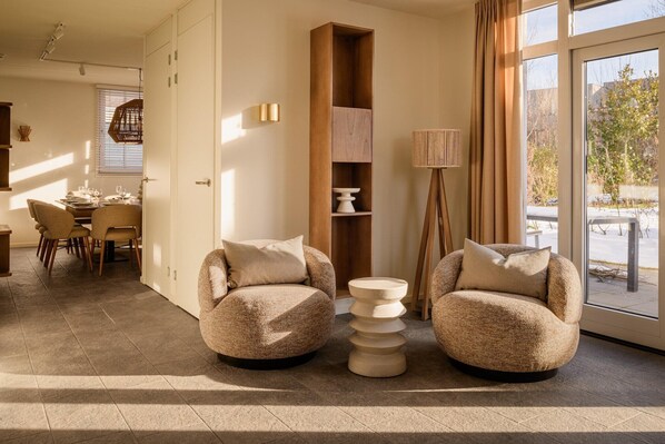 A modern living room with two round armchairs, a tall wooden bookshelf, and a floor lamp.
