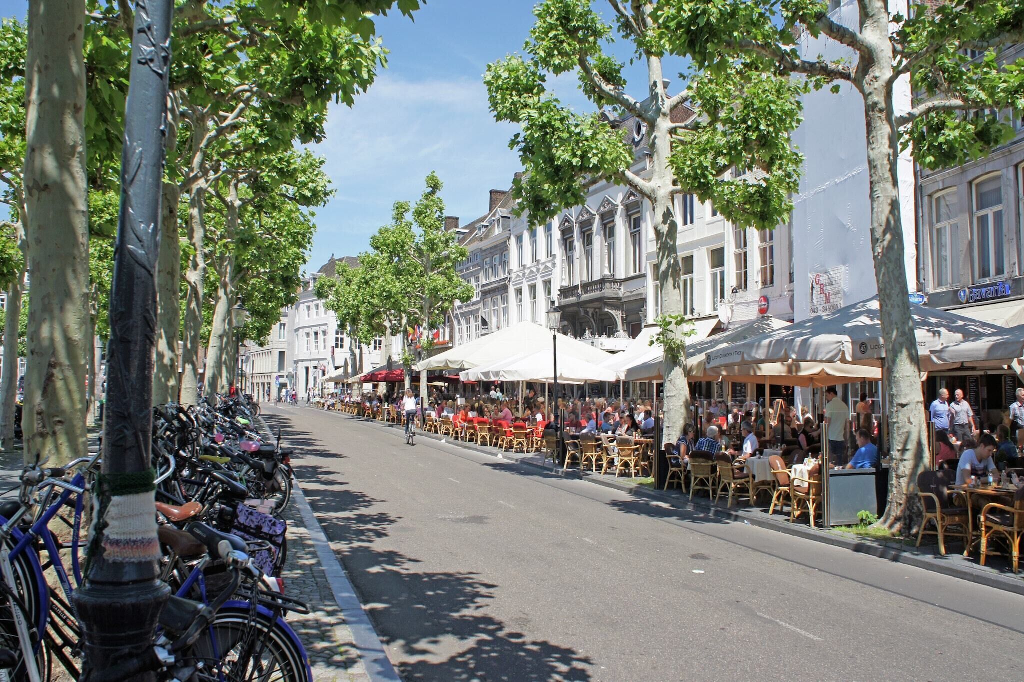 A street lined with trees and parked bicycles, with outdoor seating at cafes and restaurants.