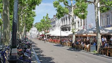 A street lined with trees and parked bicycles, with outdoor seating at cafes and restaurants.