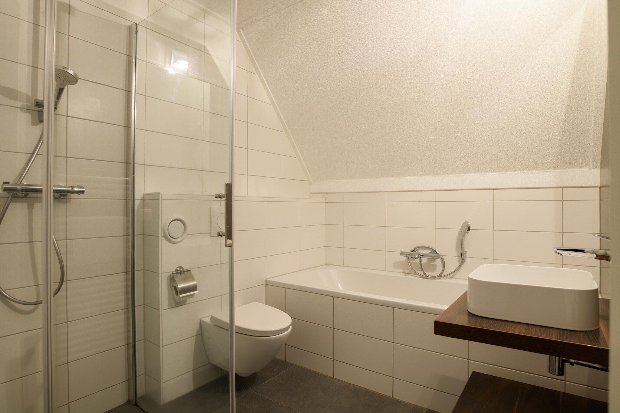 A modern bathroom with a glass-enclosed shower, a toilet, and a bathtub with a wooden vanity.