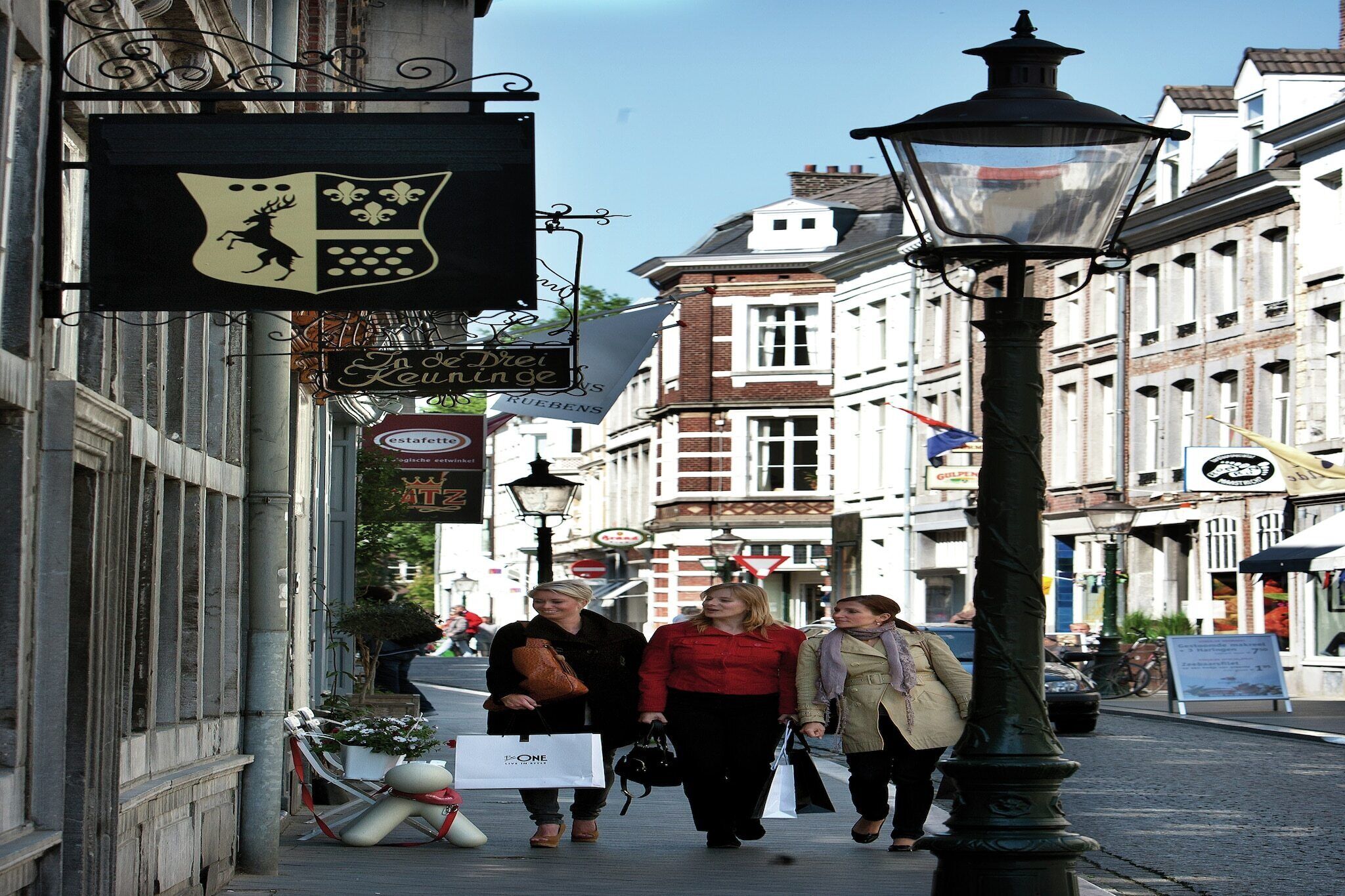 A street with historic buildings, a sign with a coat of arms, and a street lamp.