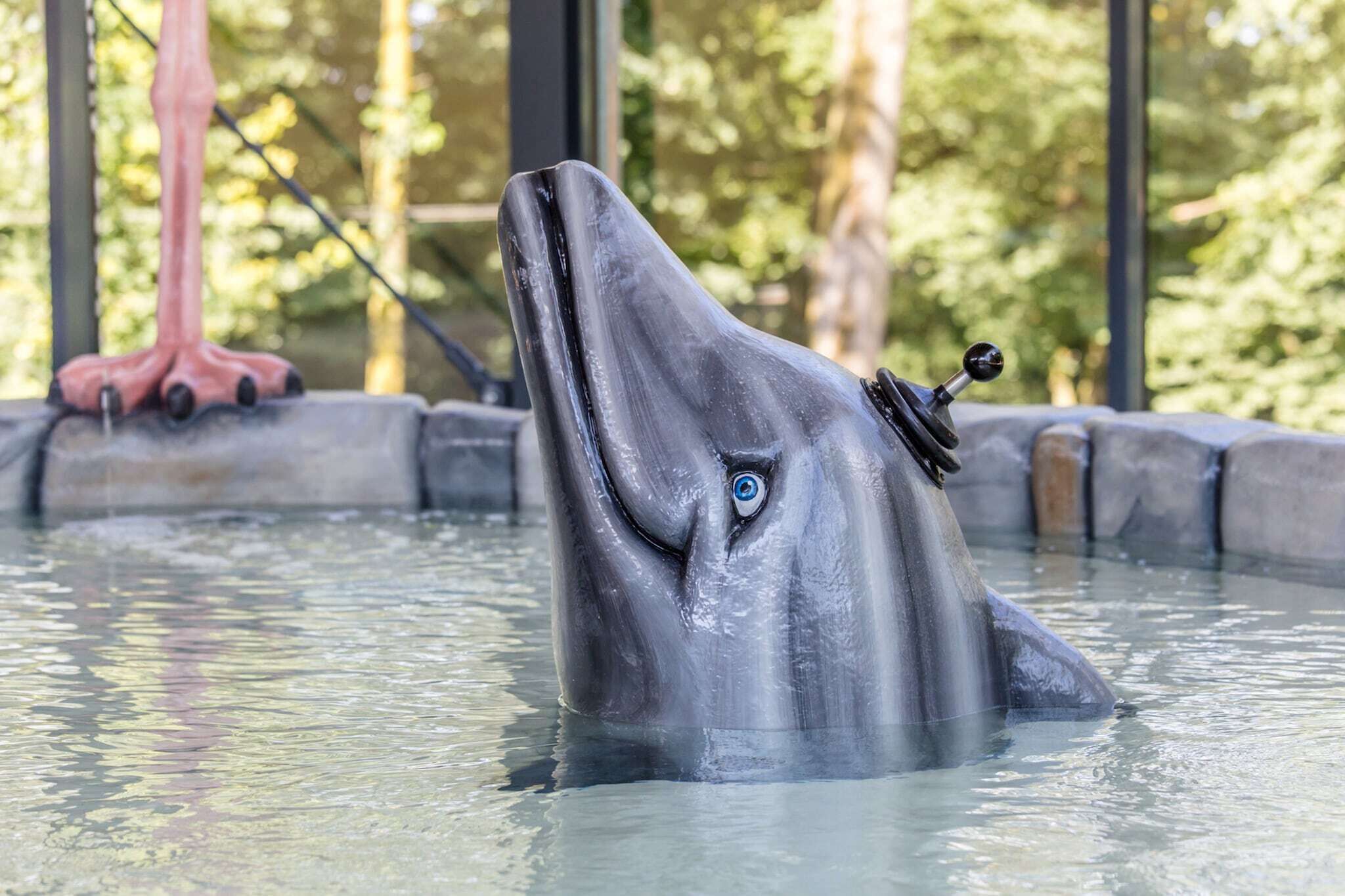 Een dolfijnbeeld in een waterpartij met een mechanische staart en een mechanisch hoofd.