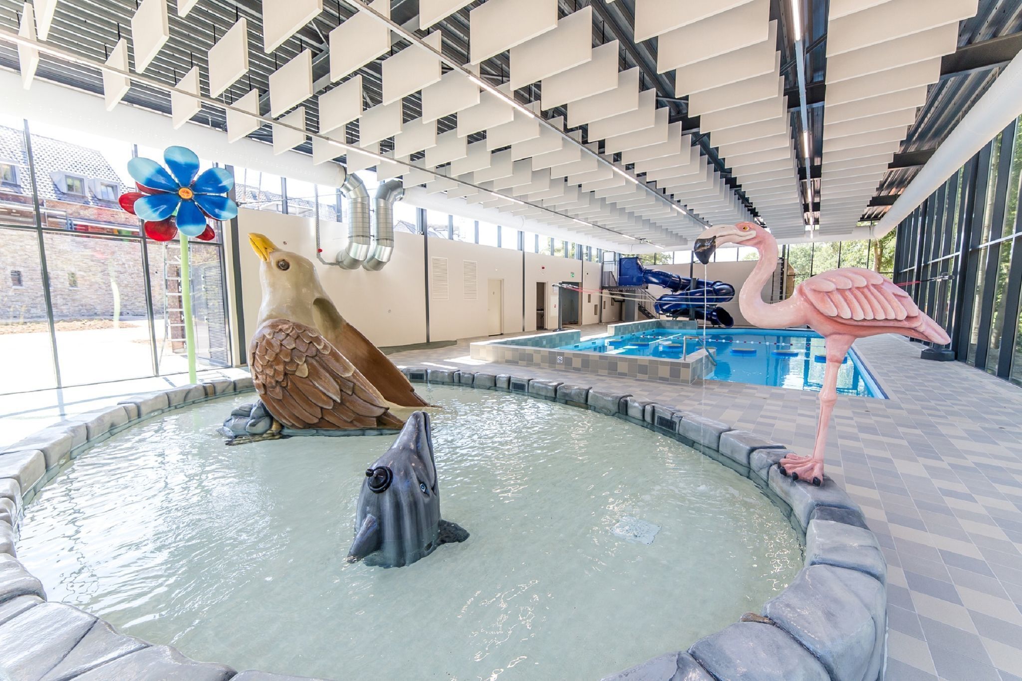 Une piscine intérieure agrémentée de sculptures d’animaux décoratives, d’une grande girouette bleue et offrant une vue sur l’extérieur grâce à de larges fenêtres.