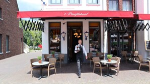 En restaurang med uteservering, ett rött markis och en servitör som bär ett bricka.