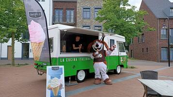 An ice cream truck with a mascot, parked in an outdoor area with brick buildings in the background.