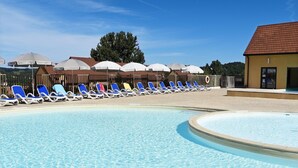 Ein Schwimmbecken mit Liegestühlen und Sonnenschirmen, umgeben von einem Holzzaun und einem Gebäude mit einem Ziegeldach.