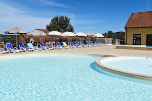 A swimming pool with sun loungers and umbrellas, surrounded by a wooden fence and a building with a tiled roof. - Holiday Home in Sarlat near Grottes de Lascaux (Sarlat La Caneda)