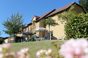 Hotellissa on ulkotila, jossa on istuimia ja aurinkovarjoja, nurmikko ja punakattoinen rakennus.