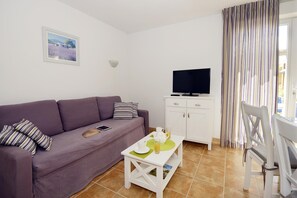Una sala con un sofá morado, un mueble blanco, un televisor y una cortina a rayas.