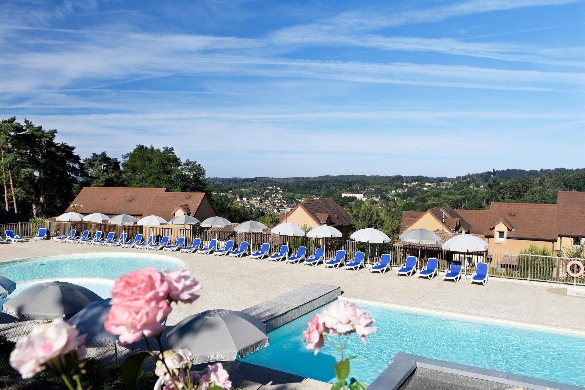 Ein Poolbereich mit Liegestühlen und Sonnenschirmen, umgeben von Gebäuden und mit Blick auf eine Stadt.