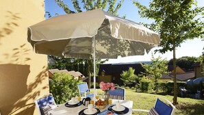Ein Essbereich im Freien mit Tisch, Stühlen und Sonnenschirm.