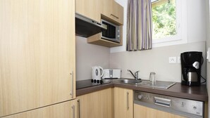 Eine kleine Küche mit Holzausstattung, einer Mikrowelle, einem Toaster, einem Wasserkocher, einer Kaffeemaschine und einem Geschirrspüler.