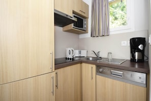 A compact kitchen with wooden cabinets, a microwave, a toaster, a kettle, a coffee maker, and a dishwasher. - Holiday Home in Sarlat near Grottes de Lascaux (Sarlat La Caneda)
