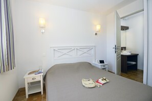 Hotellihuone, jossa on sänky, yöpöytä, lamppu ja kylpyhuone, joka näkyy avoimesta ovesta.