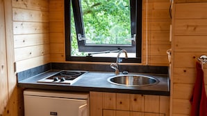 A compact kitchen with a window, a sink, a stove, and wooden cabinets. - Woodland Lodge Retreat in the Ardennes (Olloy-sur-Viroin)
