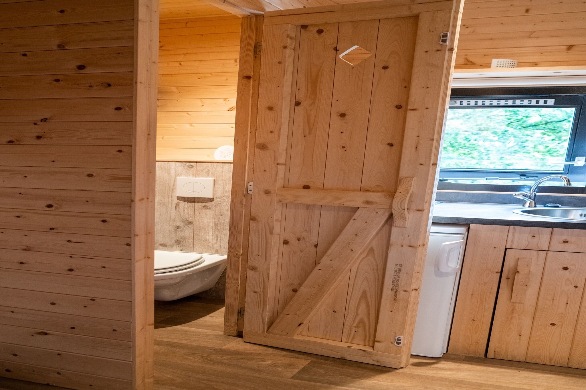 Een houten blokhut van binnen, met een houten deur naar een badkamer en een keuken.