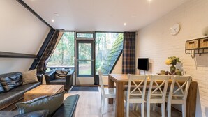 Ein stilvoller Wohnbereich mit einer Couch, einem Couchtisch, einem Esstisch mit Stühlen, einem Fernseher und einem großen Fenster mit Vorhängen.