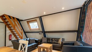 Ein Loft mit einer Holztreppe, einer Sofagarnitur, einem Couchtisch und einem kleinen Fenster.