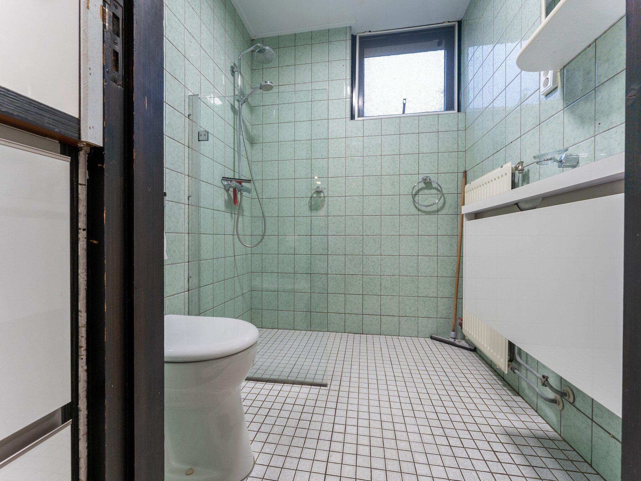 A small, tiled bathroom with a toilet, a shower, and a window.