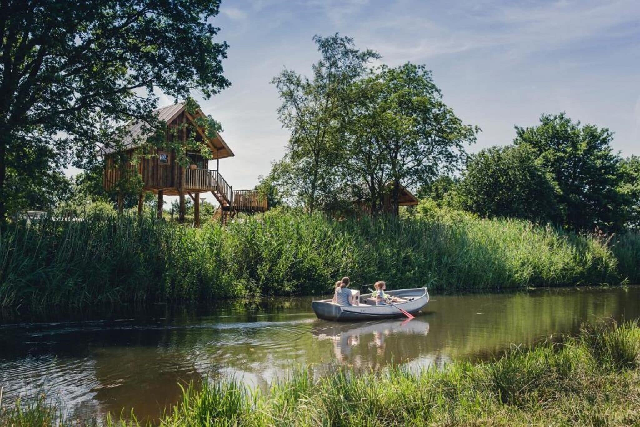 A wooden house with a deck, surrounded by lush greenery and a calm river.