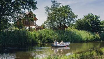 A wooden house with a deck, surrounded by lush greenery and a calm river.