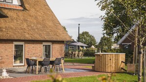 A brick building with a thatched roof, a wooden hot tub, and a patio area with tables and chairs. - Cozy Farm Stay for Groups (Zuna)