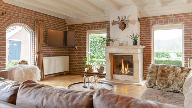 A cozy living room with a fireplace, brick walls, and a large window. - Cozy Farm Stay for Groups (Zuna)