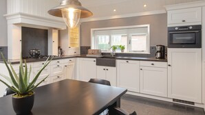 A modern kitchen with white cabinetry, a large window, and a pendant light. - Cozy Farm Stay for Groups (Zuna)