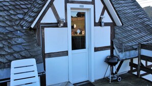 Un chalet traditionnel avec un toit à forte pente, une porte blanche et un petit espace barbecue extérieur.