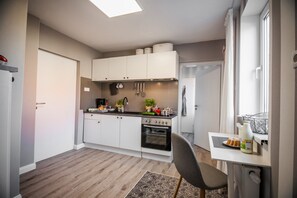 Compact kitchen with modern design, white cabinetry, and a sleek countertop, featuring a stove, oven, and sink, plus a dining area with a chair and table.