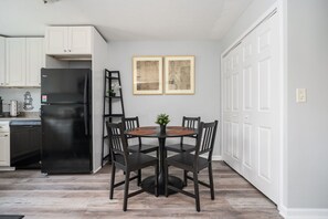 A kitchen with white cabinets, a black refrigerator, a dining table with four chairs, and two framed pictures on the wall. - [REFRESHED] Quiet & Quaint 1BR 5min to airport and 15mins to downtown (College Park)