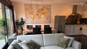 Una sala moderna con un sofá gris, una mesa de comedor con sillas, un gran mapa mundial en la pared y una zona de cocina con armarios y una estufa.