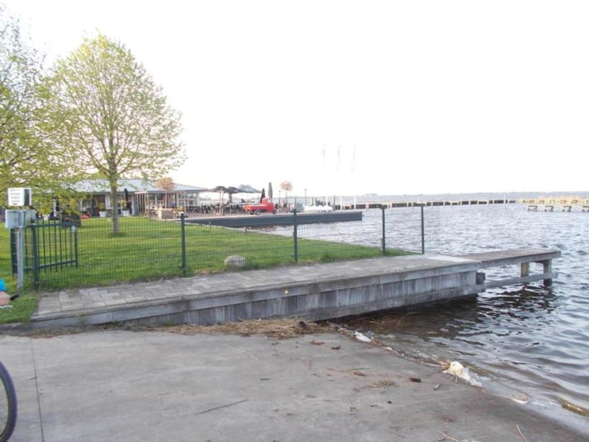 Un parque frente al agua con un camino de hormigón, una zona verde y una vista distante de un muelle.